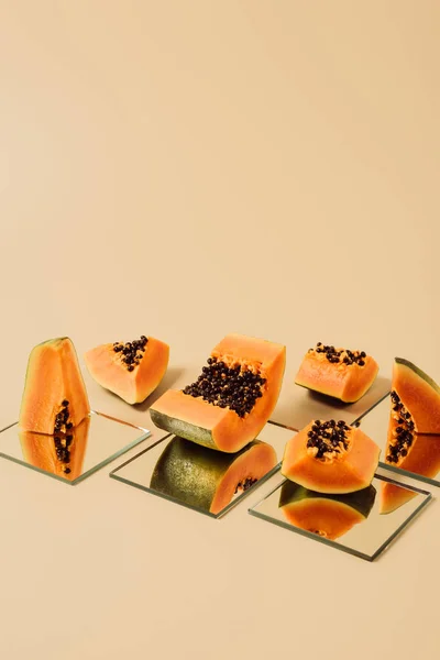 cut papayas reflecting in mirrors on beige table