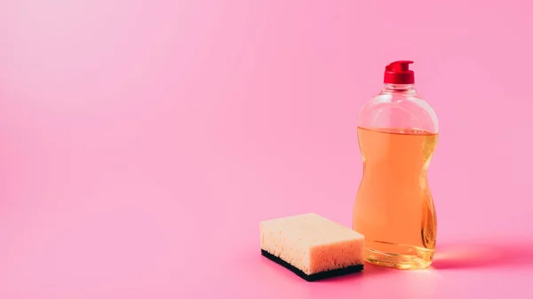 close up view of dishwashing liquid and washing sponge, pink background