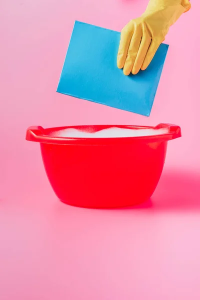 ゴム手袋をばらまくことピンクの泡 背景を持つプラスチック洗面器で粉体を洗う女性のトリミングされた画像 — ストック写真