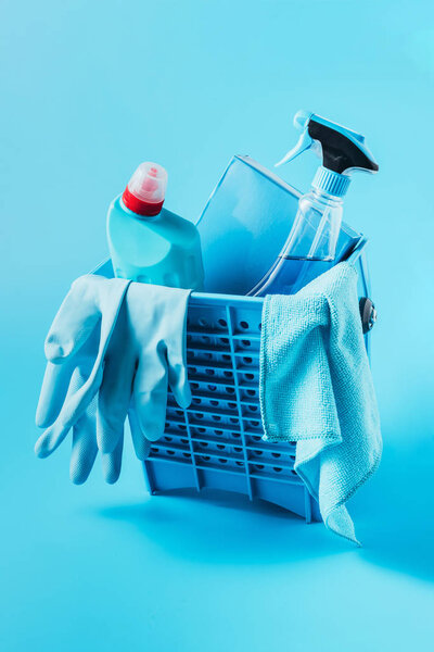 close up view of bucket with washing powder, cleaning fluids, rubber gloves and rag on blue background 