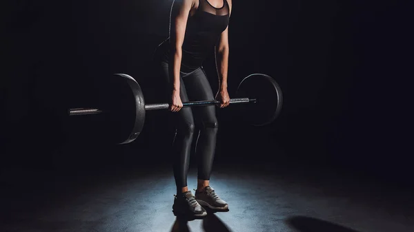 cropped image of female athlete working out with barbell at gym, black background