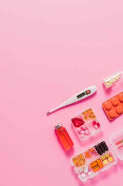 pembe üzerinde farklı ilaçlar ve elektrik termometre üstten görünüm