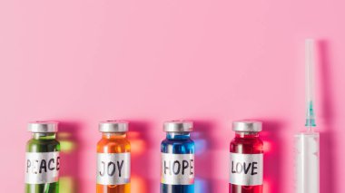 top view of syringe and bottles with love, hope, joy and peace vaccine signs in row on pink surface clipart