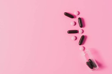dökülen pembe ve siyah hap şişeyle üstten görünüm pembe üzerinde