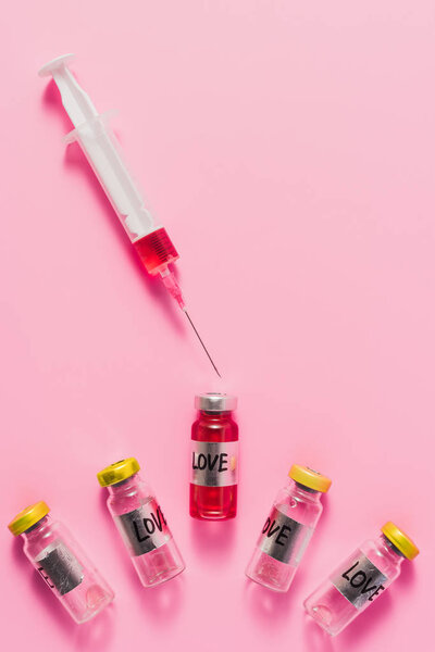 top view of syringe and bottles with love vaccine signs on pink