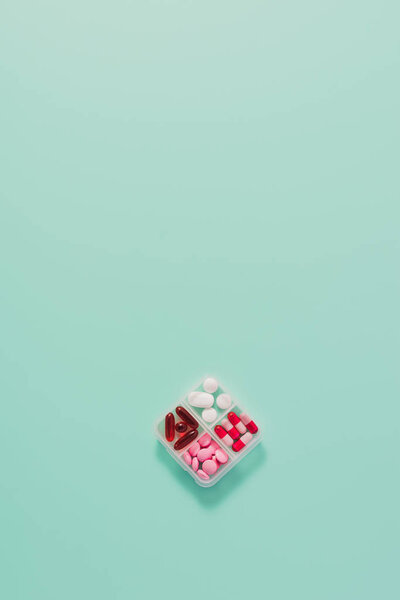 top view of plastic container with various sorted pills on blue