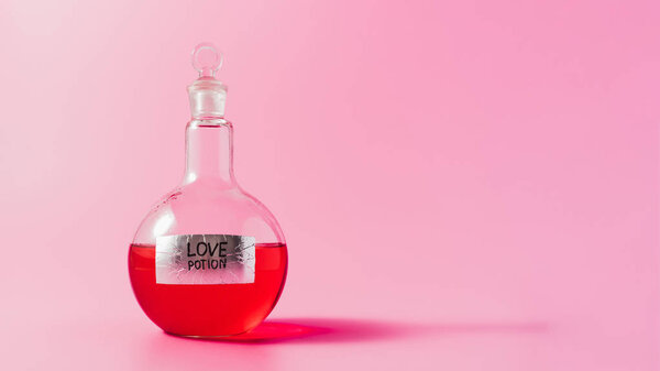 close-up shot of flask with red colored love potion on pink surface