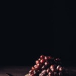 Vista de cerca de uvas rojas maduras frescas en placa vintage y cuchillo en mesa de madera en negro