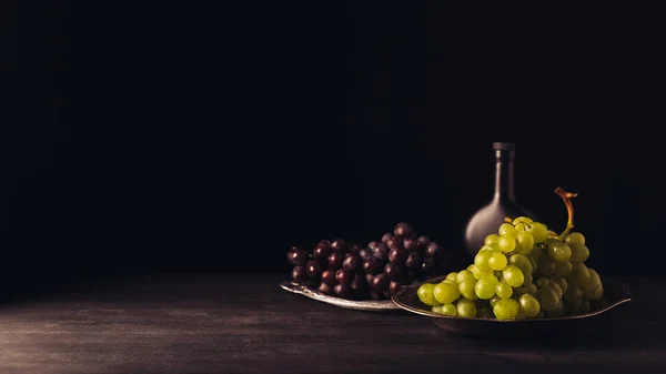 新鲜成熟的红色和白色的葡萄在盘子和酒瓶在黑色的木桌上 — 免费的图库照片