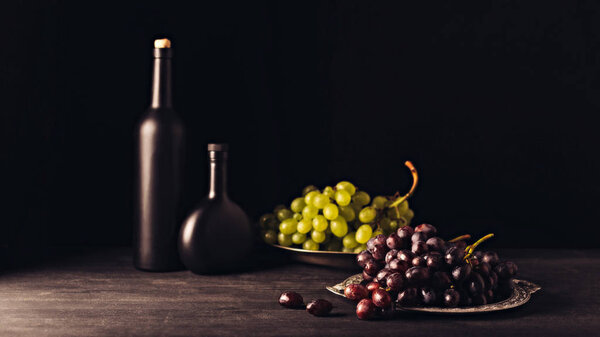delicious ripe red and white grapes on vintage plates and bottles of wine on wooden table on black