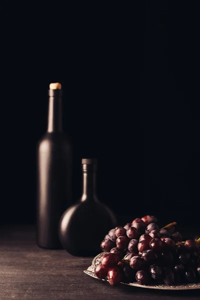 Färska Mogna Röda Druvor Och Vinflaskor Träbord Svart — Gratis stockfoto
