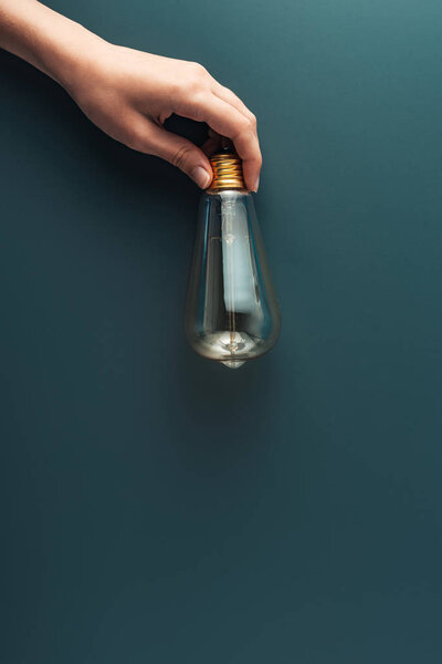 обрезанный снимок человеческой руки, держащей лампочку на сером фоне
