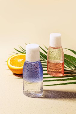 micellar su şişeleri, yeşil palmiye yaprağı ve yarım su ile damla bej zemin üzerinde turuncu görünümünü kapat