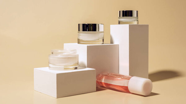 close up view of micellar water and body creams on white cubes on beige background