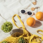 Vista de ángulo alto de gafas de sol, pendientes y bolsa de hilo amarillo con frutas frescas