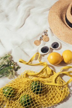 hasır şapka, güneş gözlüğü, küpe, çiçekler ve sarı dize çanta olgunlaşmış tropikal meyve ile yüksek açılı görünüş