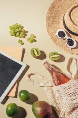 güneş gözlüğü, şapka, içecek ve meyve ile dijital tablet ve dize çanta üstten görünüm 