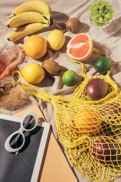 верхний вид цифровой планшет, солнцезащитные очки и желтая струна мешок со свежими спелыми тропическими фруктами
