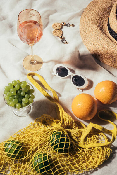 top view of wicker hat, sunglasses, earrings, glass with summer beverage and string bag with fresh fruits
