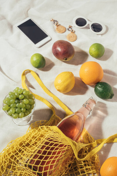 high angle view of smartphone, sunglasses, earrings and string bag with fresh fruits