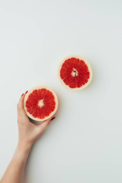 partial view of woman holding grapefruit halves, on grey