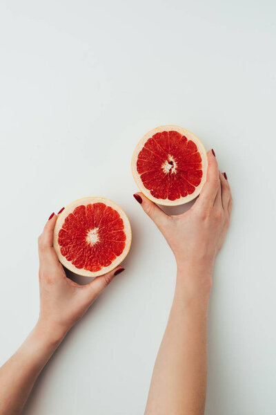 cropped view of woman holding grapefruit halves, on grey