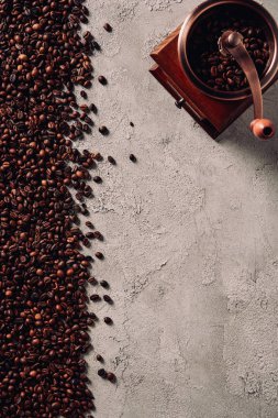 top view of spilled coffee beans with vintage grinder on concrete surface clipart