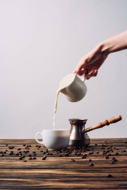 cropped shot of woman pouring milk into coffee on rustic wooden table clipart