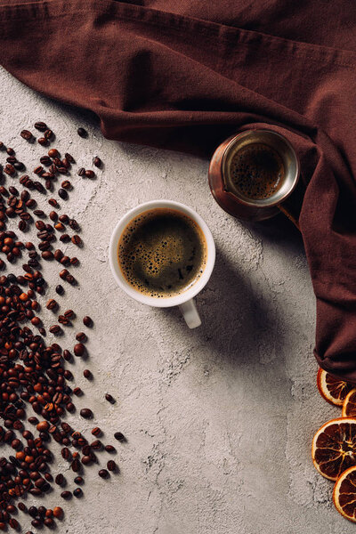 top view of cup of coffee with cezve and coffee beans on concrete surface