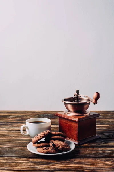 cup of coffee with vintage grinder and chocolate chip cookies on rustic wooden table
