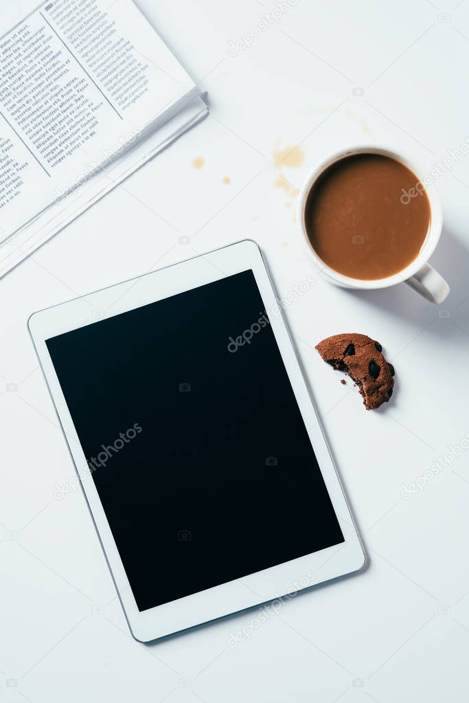 top view of tablet with coffee cup and bitten chocolate chip cookie on white surface