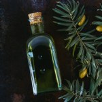 Top view of bottle of tasty olive oil, twigs and olives on shabby surface