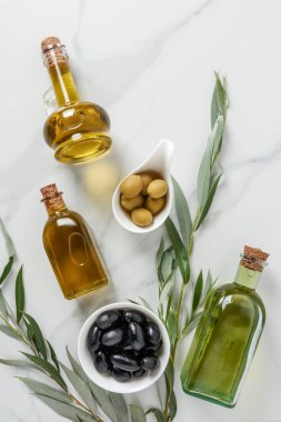 top view of olive oil in glass bottles and tasty olives on marble table clipart