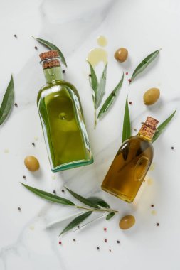 top view of two bottles of olive oil and twigs on marble table clipart