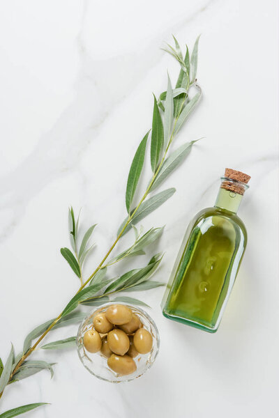top view of bottle of olive oil and olives in bowl on marble table