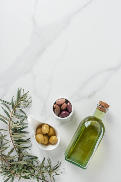 top view of olive oil and yummy olives in bowls on marble table 