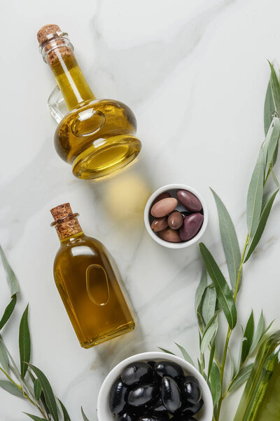 top view of olive oil in glass bottles and olives on white surface