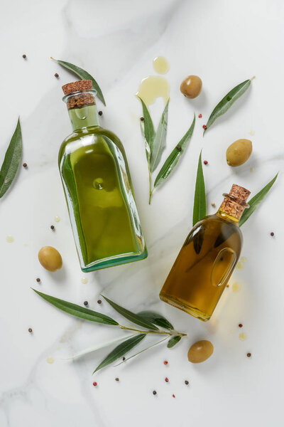 top view of two bottles of olive oil and twigs on marble table