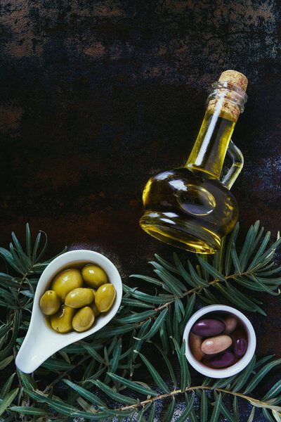 top view of yummy olives in bowls and bottles of olive oil on shabby surface