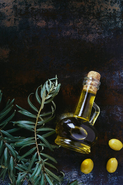 top view of bottle of olive oil, twigs and tasty olives on shabby surface