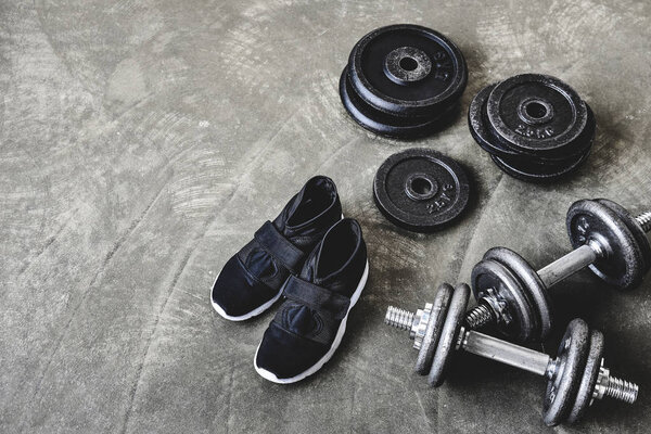 high angle view of dumbbells with weight plates and sneakers on concrete floor