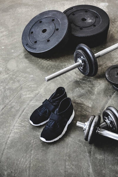 dumbbells and barbell with weight plates and sneakers on concrete surface