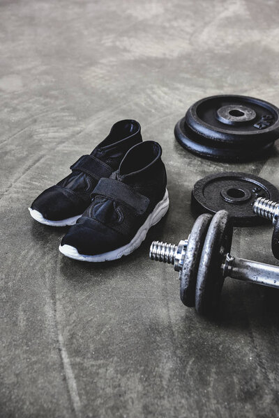 close-up shot of dumbbells with weight plates and sneakers on concrete floor