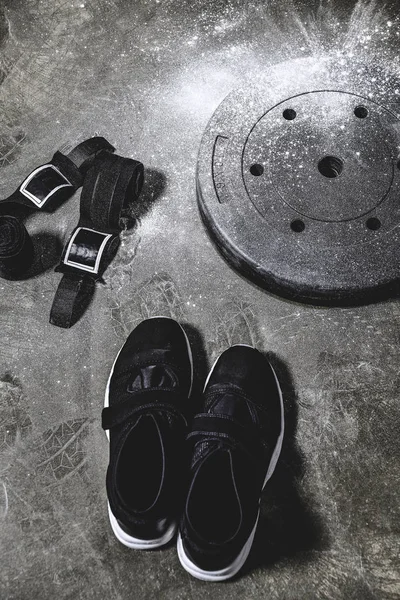 sneakers with wrist wraps and weight plate covered with talc on concrete surface