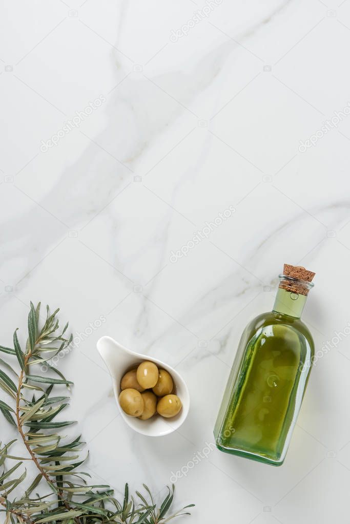 top view of bottle of olive oil and olives in bowl on marble surface