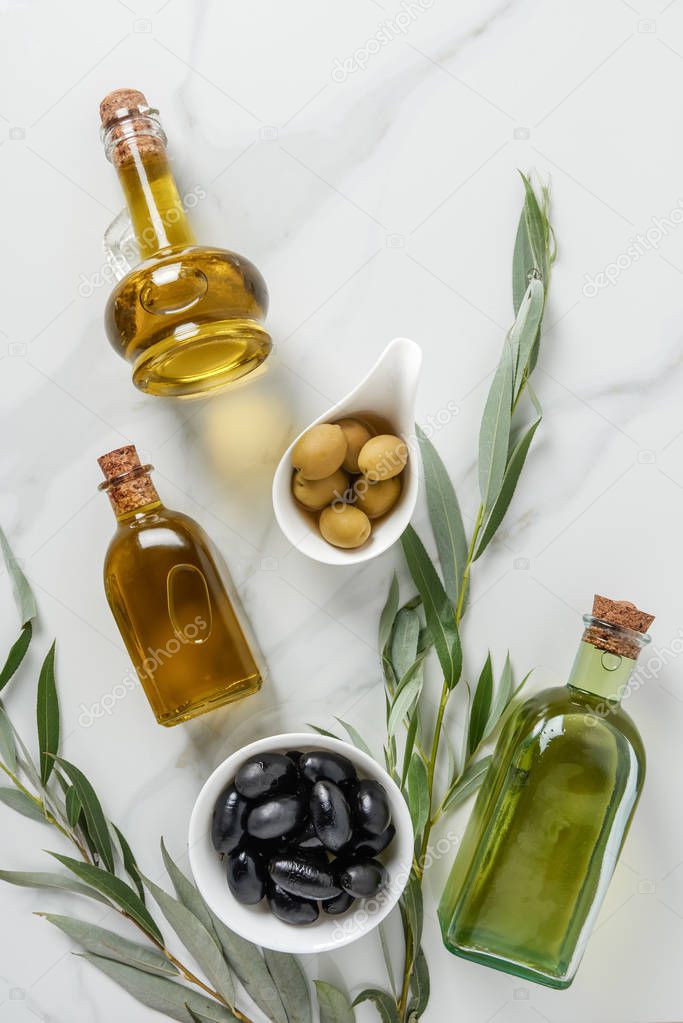 top view of olive oil in glass bottles and tasty olives on marble table