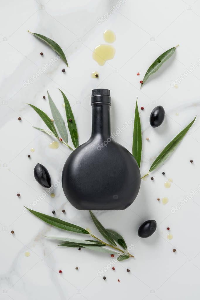 elevated view of black bottle of olive oil and olives on marble table