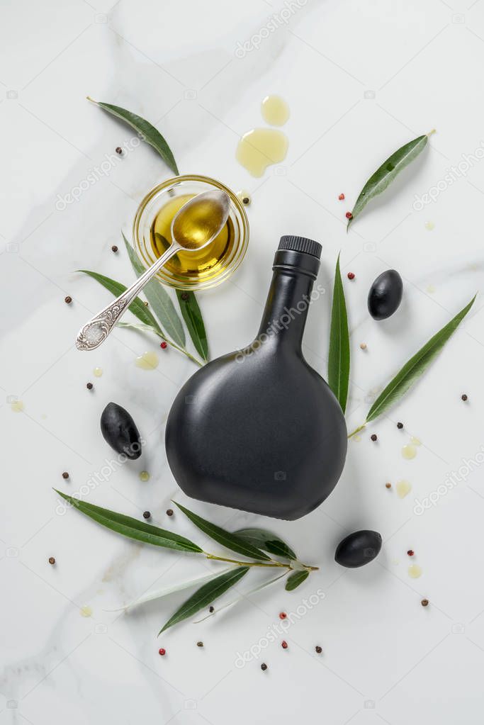 top view of black bottle of olive oil and glass with spoon on marble table