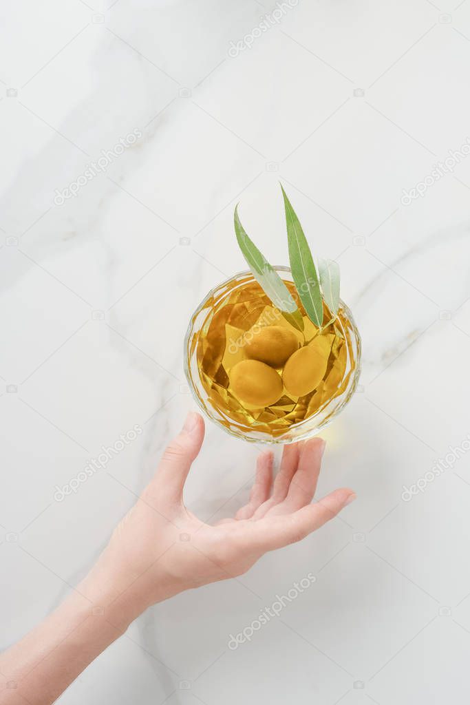 cropped image of woman reaching hand to glass of olive oil on marble table