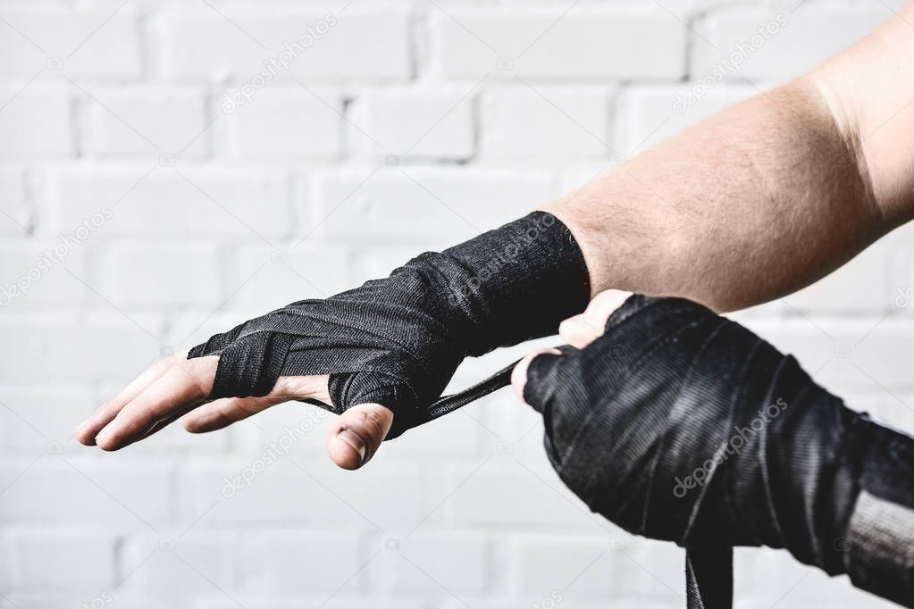cropped shot of weight lifter wrapping hands before workout in front of white brick wall